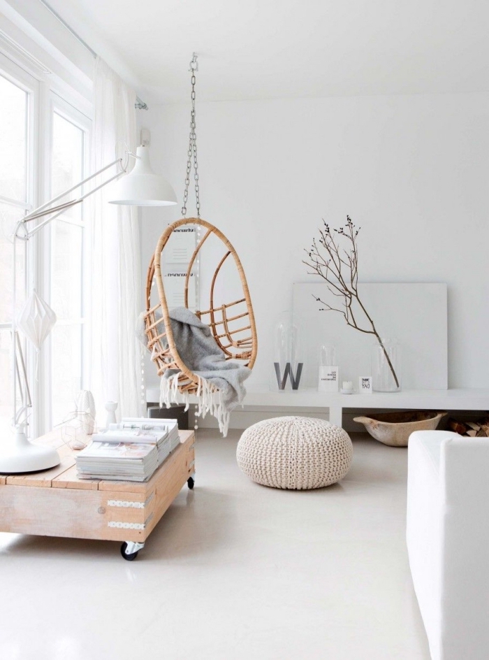 intérieur blanc cocooning dans un salon de style scandinave épuré avec une balançoire d'intérieur en rotin et un pouf tricoté