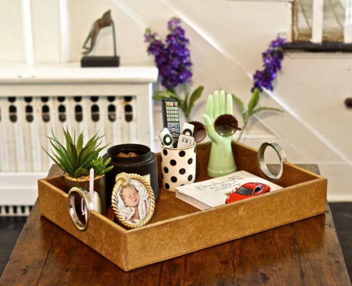 plateau de bois et objets accumulés, petite photo de bébé avec encadrement rond, pot de fleur, tasse pointillé, sculpture avant-garde