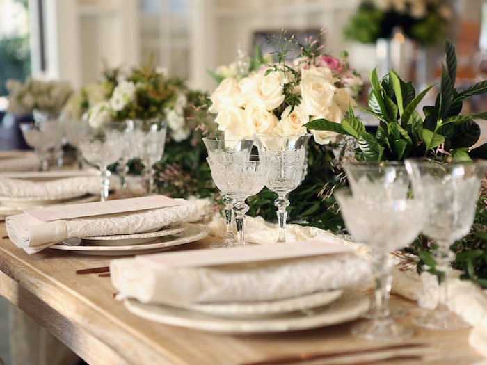 composition florale de mariage en guise de centre table et chemin de table dentelle blanche, pliage simple en rectangle dentelle sur table bois rustique
