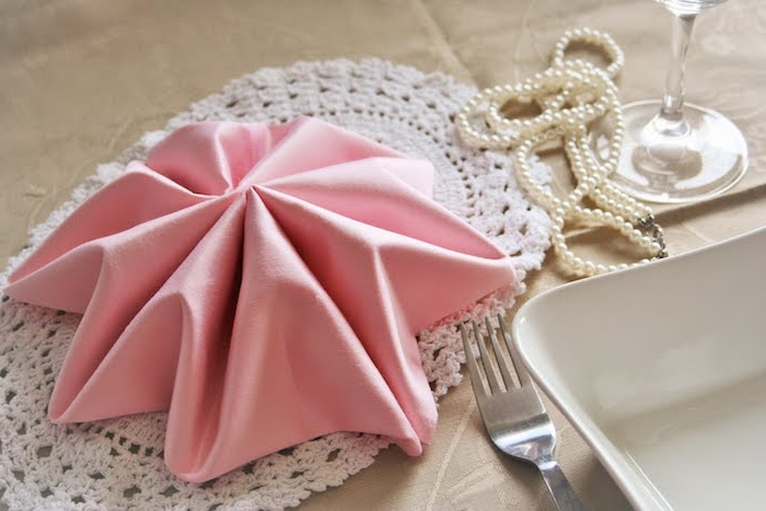 comment plier une serviette tissu rose en forme d étoile sur napperon blanc, deco mariage collier de perles, couverts et vaisselle simple