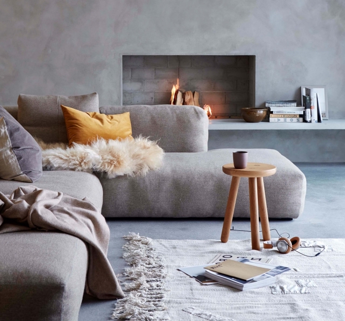de la simplicité et de la douceur dans ce salon gris aux murs effet béton avec une cheminée encastrée et un grand canapé cosy