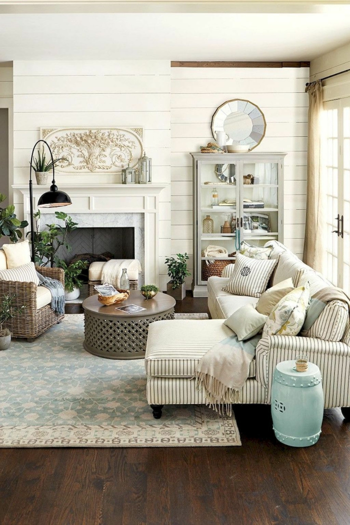 tapis bleu, table basse ronde, sofa d'angle beige, miroir fenêtre, buffet blanc, lambris mural blanc, cheminée, salon déco campagne chic