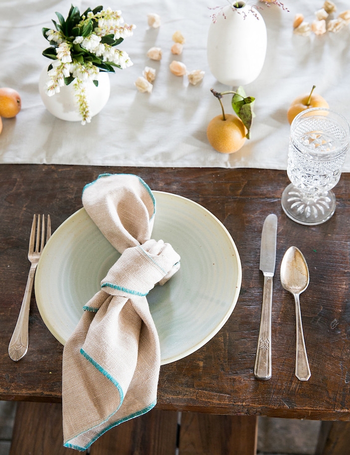 idee originale de chemin de table tissu blanc décoré de petits bouquets de fleurs et pommes, table rustique bois brut, serviette en noeud marin