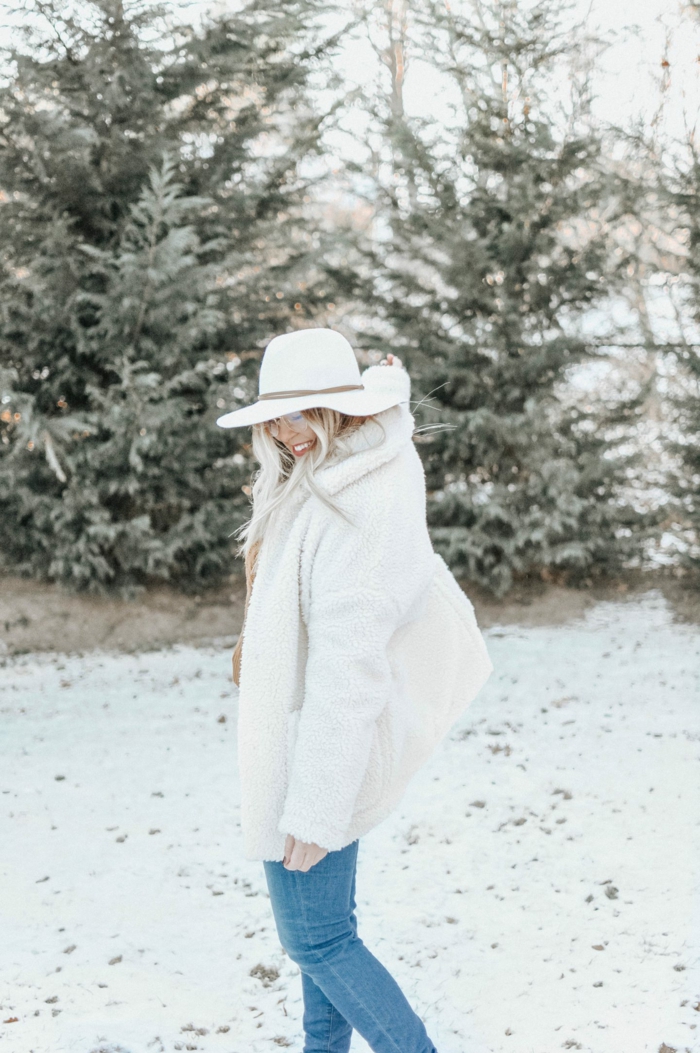 femme dans la forêt, manteau poilu blanc, jeans bleus, pins enneigés, paysage d'hiver