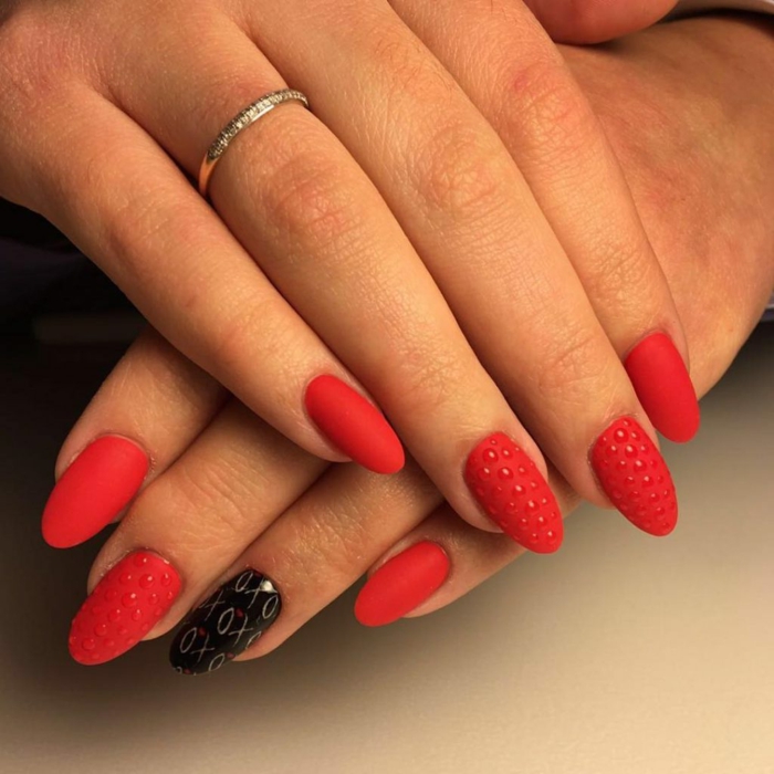 ongles ovales couleur rouge, motifs 3d sur l'ongle, bague fine en métal, ongles mi-longs forme classique