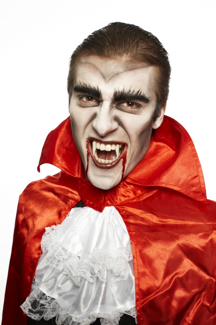 vampire avec des fausses dents de vampire et pèlerine orange, lèvres sanglantes avec faux sang