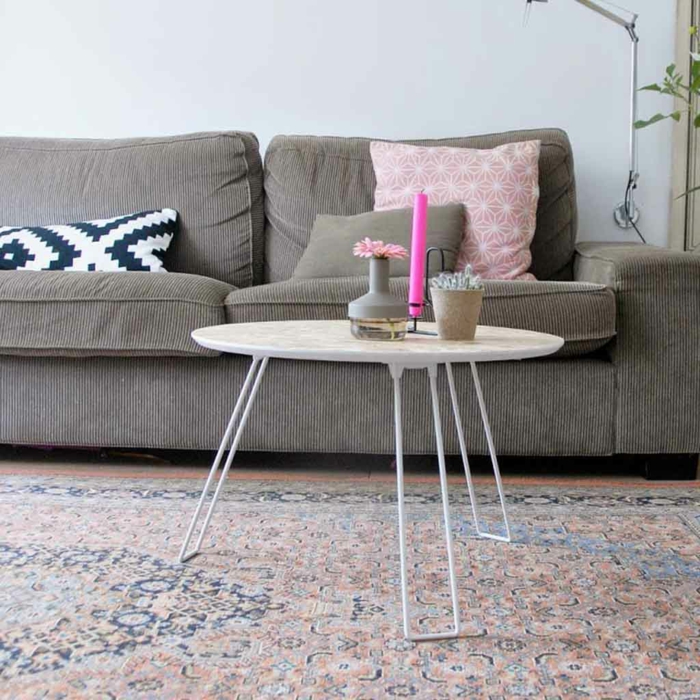 table basse ronde, bougie rose, vase gris avec petite fleur, tapis persan aux couleurs pastels, sofa gris, coussins décoratifs, peinture murale grise