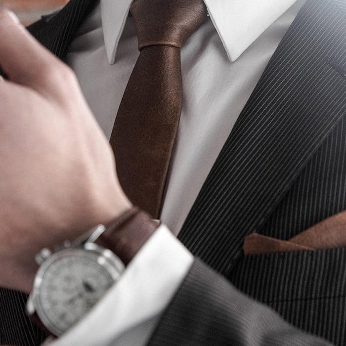 photo de cravate en cuir marron assortie à montre et pochette sur smoking noir gris rayé et chemise blanche