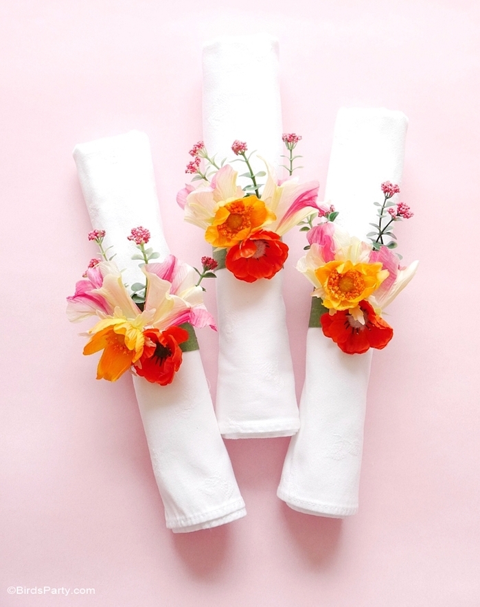 serviettes enroulées avec un anneau en bande de tissu décorée de fleurs artificielles colorées pour votre mariage theme floral