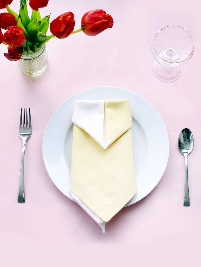 table mariage avec assiette blanche et idée intéressante de pliage de serviette en papier deux couleurs, deco en bouquet de tulipes rouges