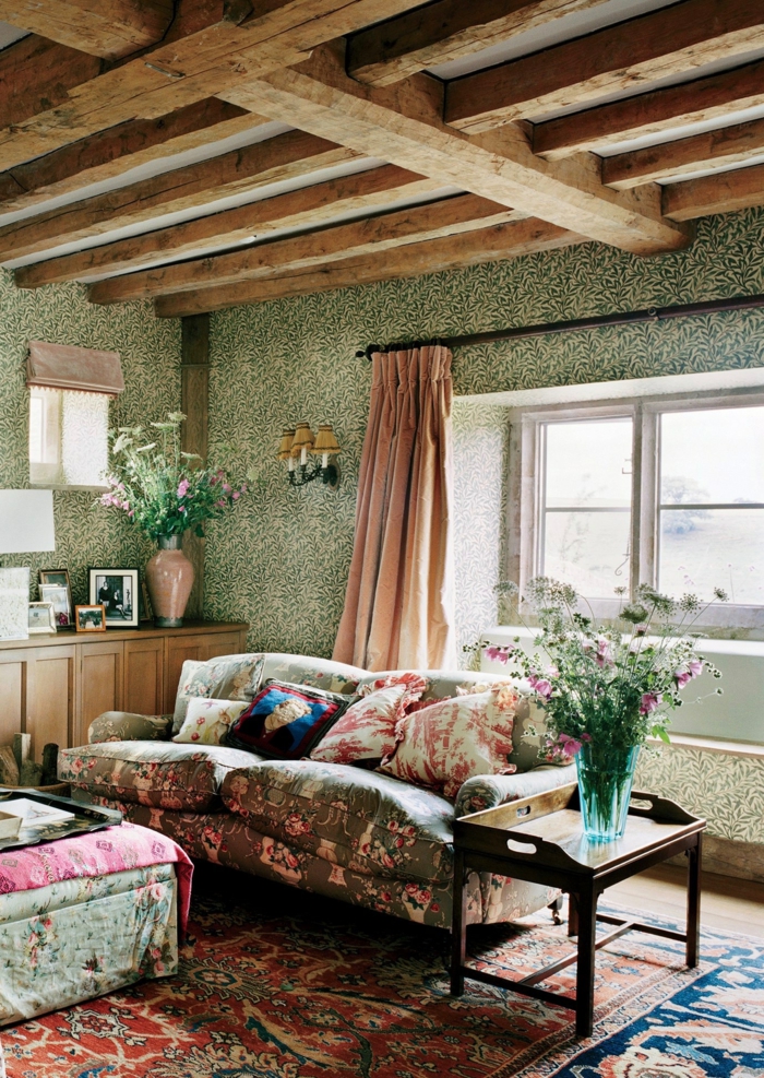 déco maison de campagne, sofas floraux, ottoman au tapissier rustique, poutres en bois, rideau rose, vase en verre avec fleurs des champs