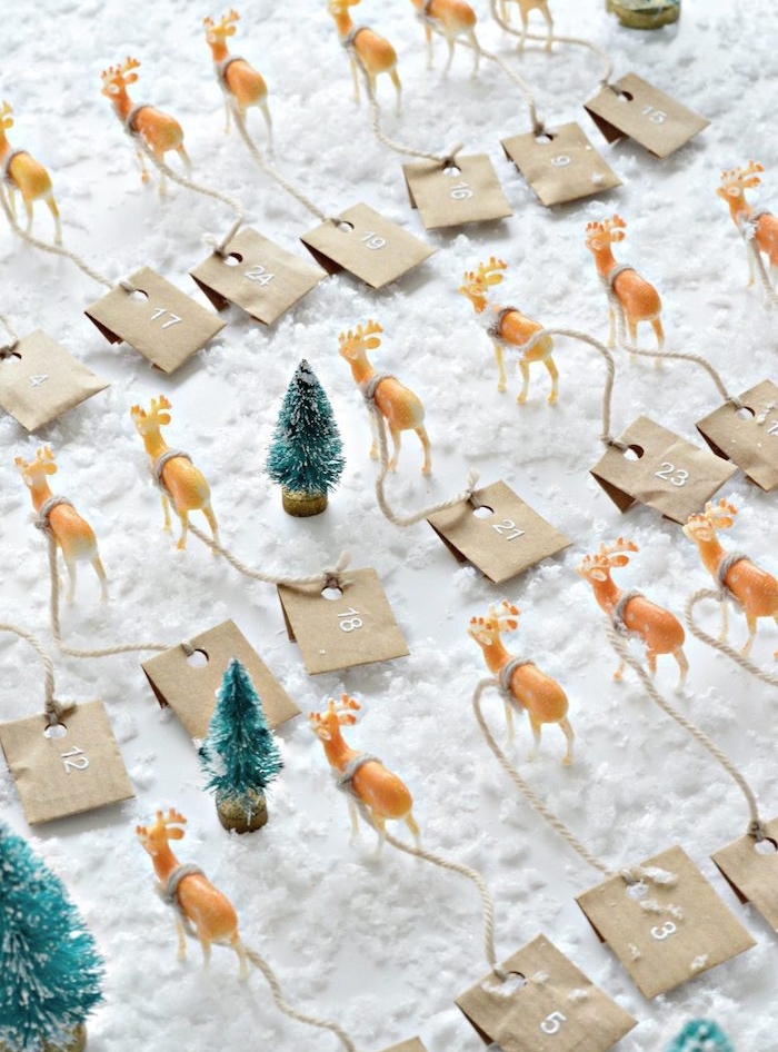 calendrier de l avent en petites figurines de cerfs, rennes de noel avec de petits sachets kraft accrochés, figurines de sapins sur neige artificielle