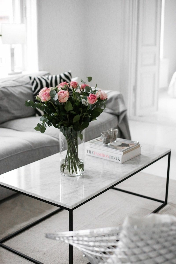 table basse marbre et fer, vase avec roses, livres blancs, sofa gris, intérieur gris clair, petits bougeoirs