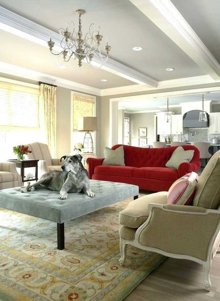 tapis persan, chandelier épuré, sofa rouge, grand ottoman gris clair et chien gris, salon cosy déco campagne esprit brocante
