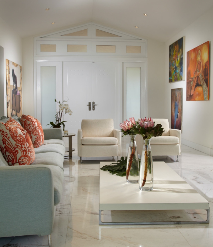 salle de séjour blanche, sofa gris clair, coussins aux motifs floraux, deux vases de verre avec des fleurs, tableaux peintures