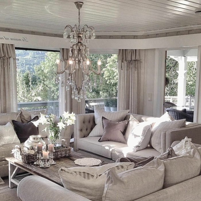 sofas gris clair, table basse en bois, bougeoirs argentés, grand plafonnier cristal, coussins beiges et taupe