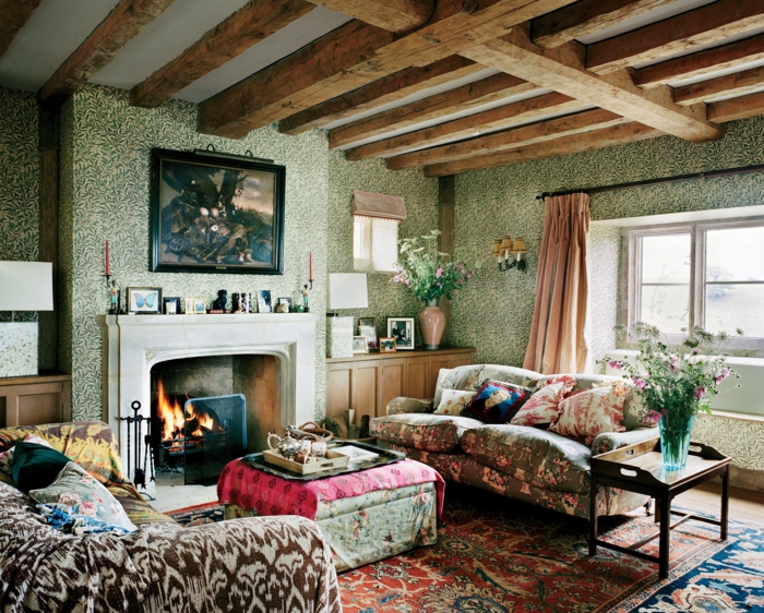 salon motifs colorés, ottoman, cheminée, papier peint vert, plafond en poutres, sofa shabby bariolé, tapis persan, cheminée