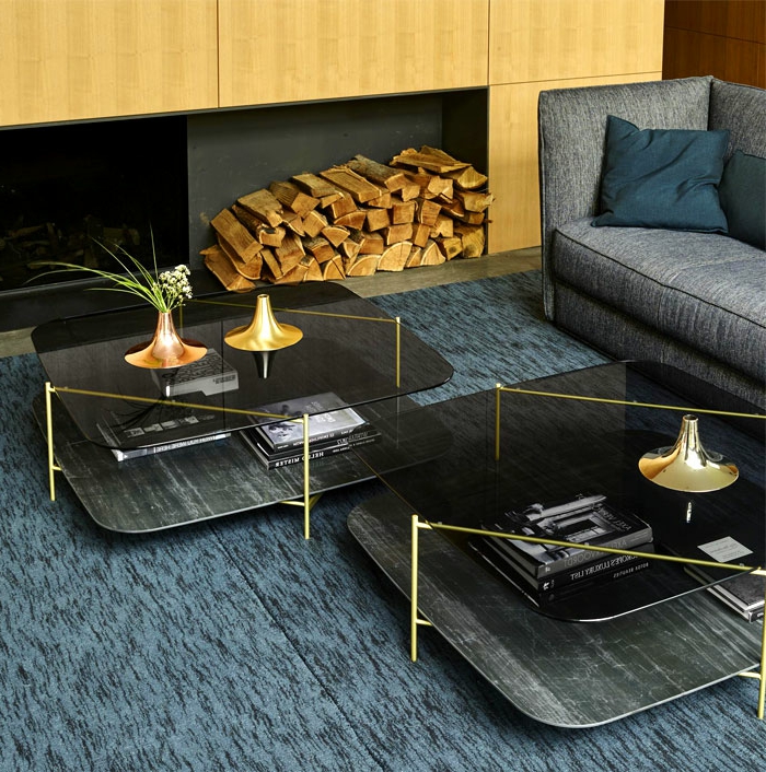 deux tables au piétement doré et plateau de verre, tapis bleu, sofa gris, range-bûches, coussin couleur pétrole 
