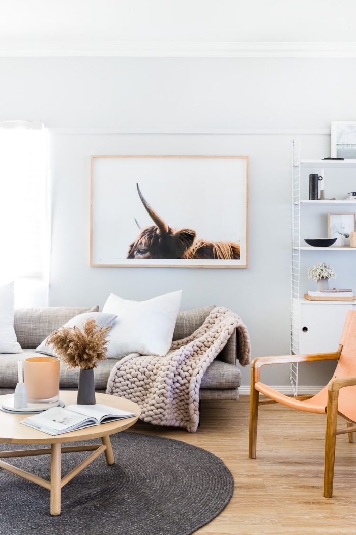 deco cocooning dans un salon de style scandinave vintage en tons neutres, canapé beige avec plaid grosse maille enveloppante, surmonté d'un cadre photo aux couleurs harmonisant avec le décor