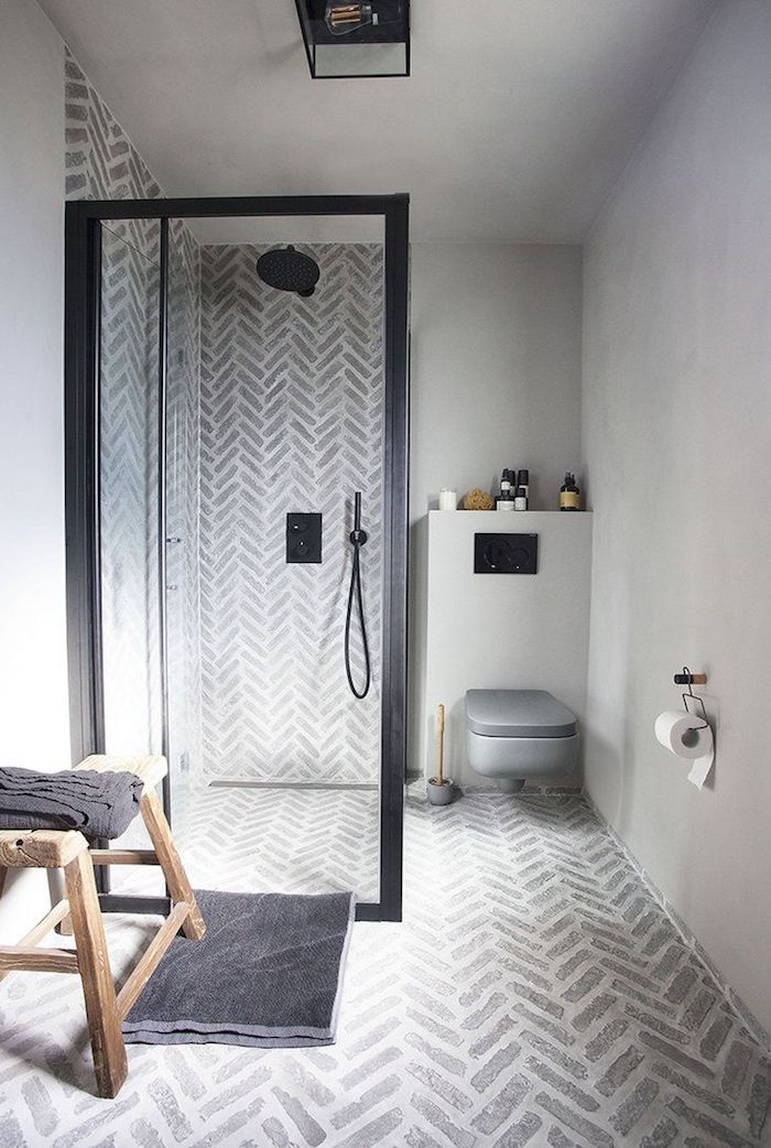 salle de bain en béton ciré avec mur en ciment gris sur le sol et douche italienne avec paroi noire et petit banc en bois rustique