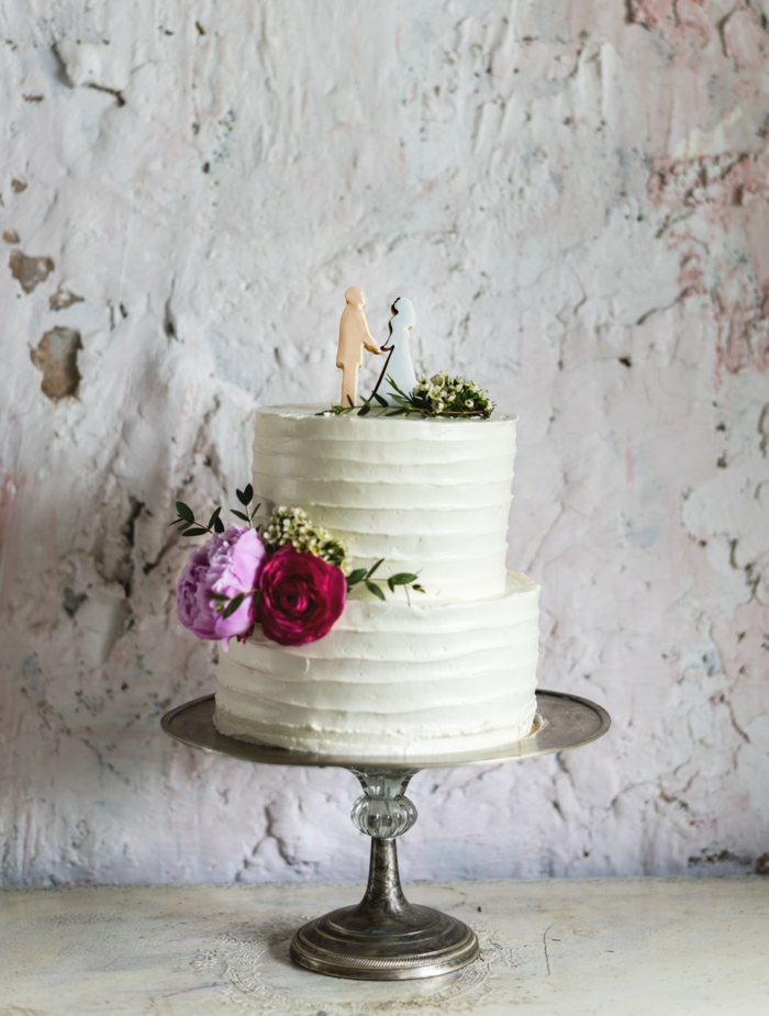 Beau gateau de mariage simple en blanc avec quelques fleurs pour décoration et silhouettes des mariés pour figurines de gateau mariage