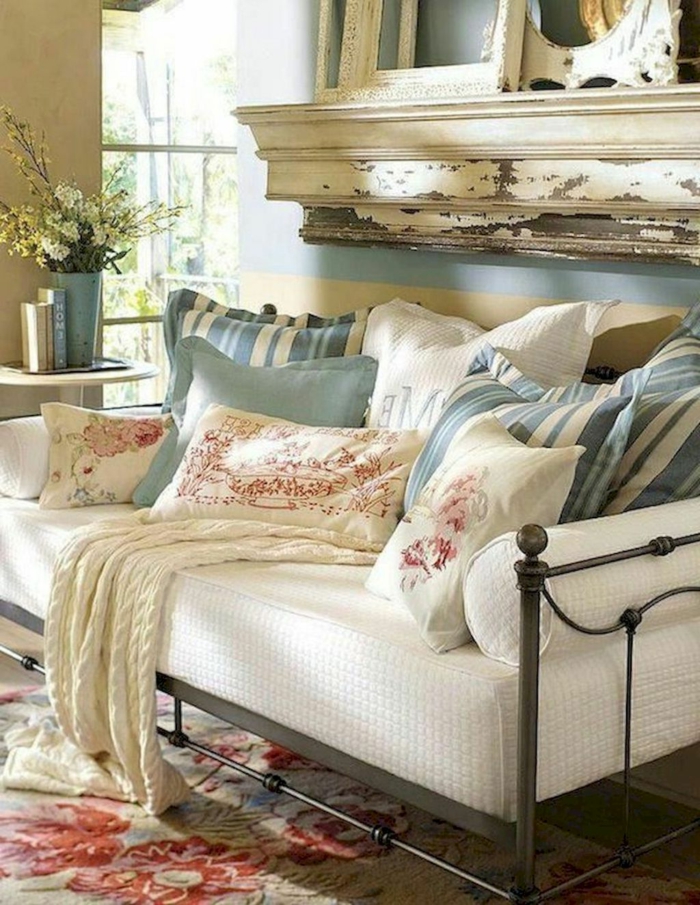 sofa blanc, tapis persan, coussins rayés, plaid tricoté couleur crème, mur bleu, vases, cadres vieillis