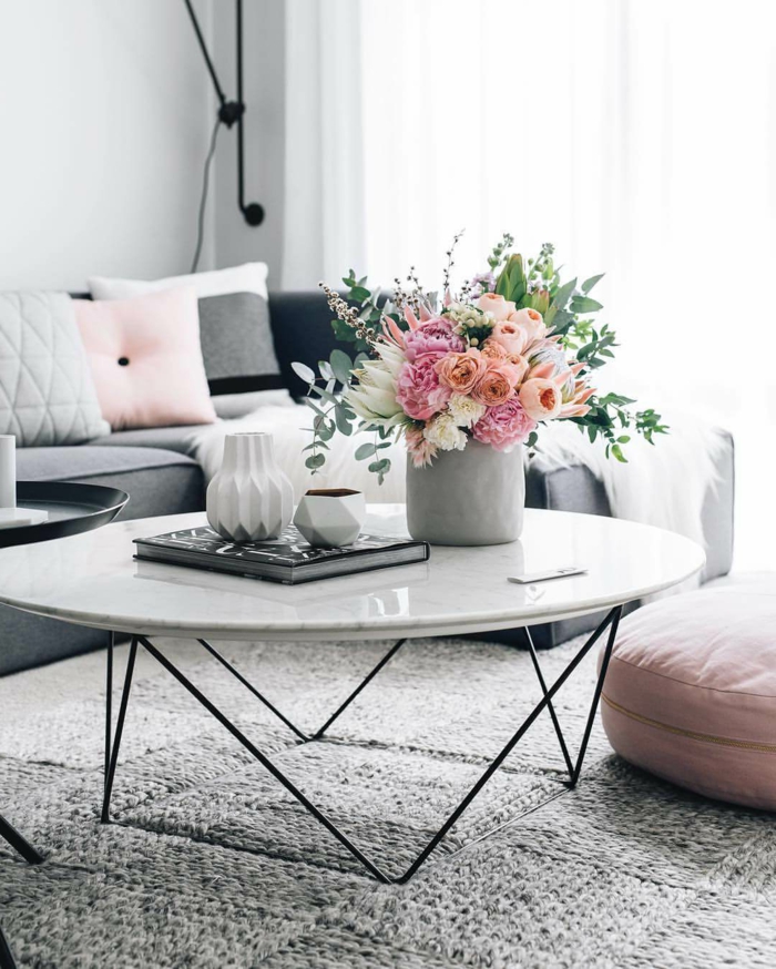 tapis gris matériel naturel, table basse ronde, grand vase avec bouquet champêtre, tabouret rose, sofa et coussins pastels