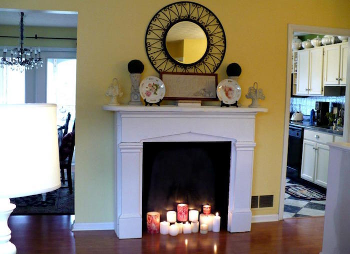 cheminée décorative avec manteau simple blanc dans salon mur jaune et lot de bougies dans insert à fond noir