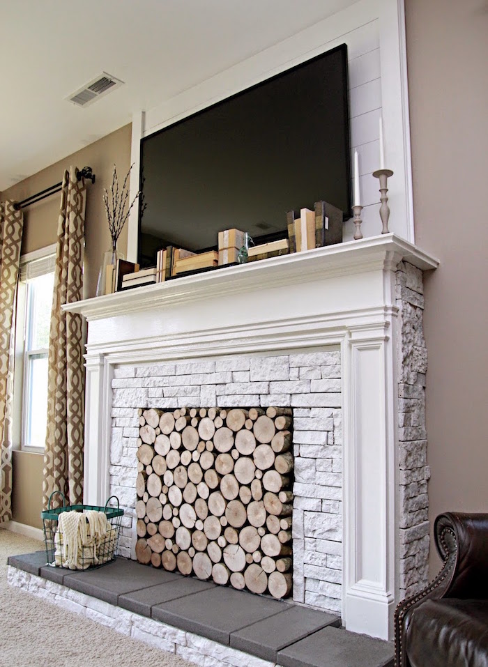 cheminée décorative fausse en pierres blanches comme support tv et foyer rempli de buches en bois 