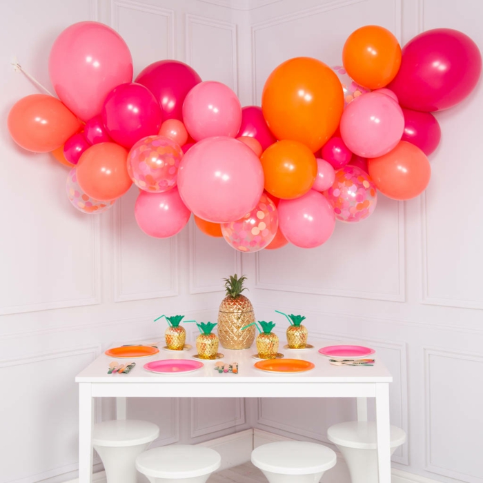 table basse blanche décorée d'assiettes colorées, ballons regroupés ensemble en forme d'arche et suspendus au mur