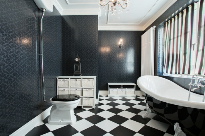 carrelage damier noir et blanc, grande baignoire en fonte, rideaux et grande fenêtre, plafond blanc, meuble de rangement blanc, mur en carreaux gris