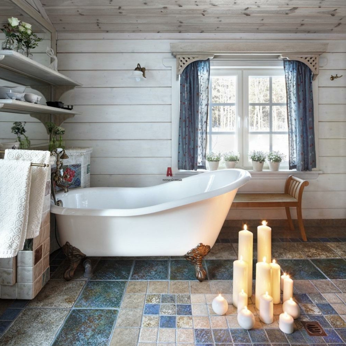salle de bain en bleu et blanc, bougies allumées, sol mosaique rideaux bleus, étagères blanches, baignoire sabot blanche, murs en lambris blanc