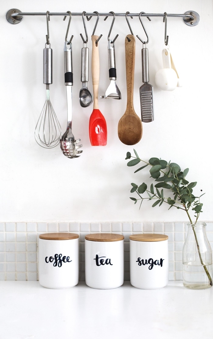 une barre métallique murale avec crochets pour suspendre ses ustensiles de cuisine, trois pots blancs avec couvercles en liège pour le café, le thé et le sucre