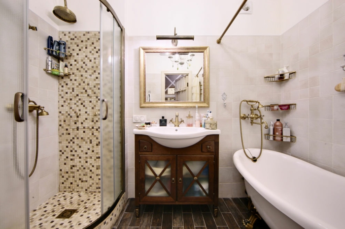 baignoire ovale, cabine de douche, parois en verre, grande tête de douche, miroir carré encadré, meuble sous vasque en bois, sol en planches 