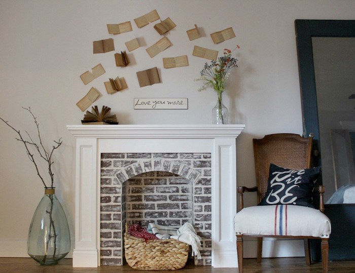 fausse cheminée déco avec manteau imitation briques avec panier deco dans foyer avec mur blanc et pages de livres anciens collées sur le mur