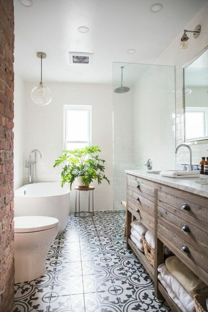 salle de bain au sol carreaux de ciment, meuble en bois, tiroirs et rangement de serviettes, tabouret, plante verte, murs peints blancs, mur en briques
