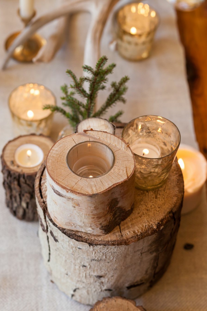 déco de table pour Noël en troncs de bois, bougies allumées, brin vert de pin, centre de table