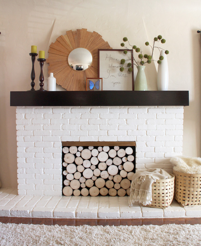 faux manteau cheminée décoratif en briques blanches aec buches bois dans foyer moquette beige sur le sol et objets deco style ambiance scandinave