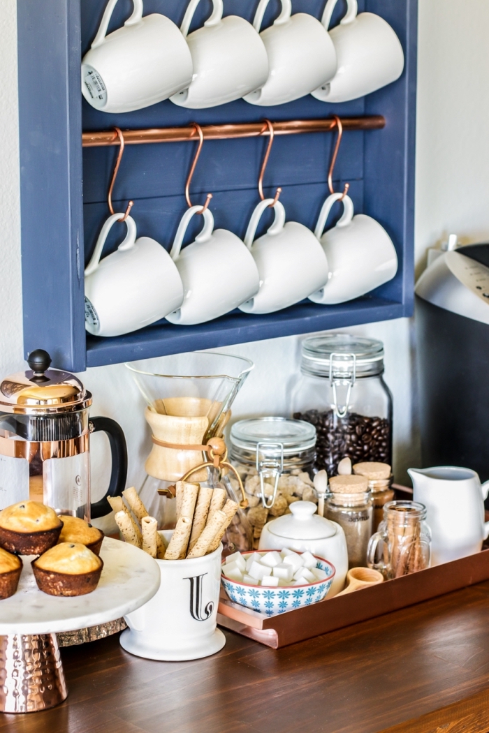 une étagère murale avec barres en cuivre et des crochets qui sert d'un support pour les tasses à café, coin café aménagé sur un bout du comptoir en bois