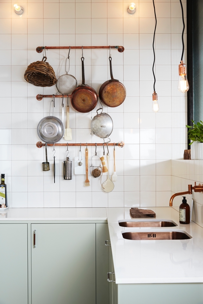 astuce deco pour aménager une cuisine fonctionnelle de style bistrot, cuisine scandinave vintage en blanc et vert amande aux accents en cuivre, des porte-ustensiles de cuisine avec des tuyaux en cuivre fixés au mur