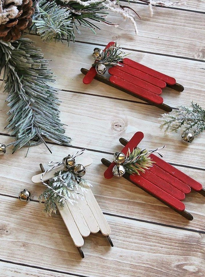 petit traineau en batonnets de glace rouge et sans couleur avec deco branches de pin et clochettes, décoration de Noël à fabriquer pour adultes