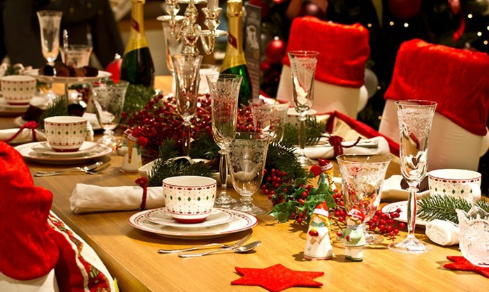 table longue en bois, assiettes blanches et tasses à café motifs colorés, sous assiettes étoiles rouges, verres à vin, déco verte, bouteille de champagne