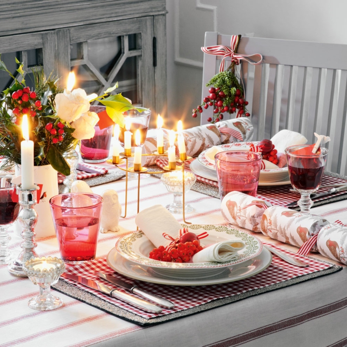 table décorée pour Noel, sous assiettes aux carreaux, tasses roses transparentes, porte bougies doré, bougies blanches, chaise gris clair et baies rouges