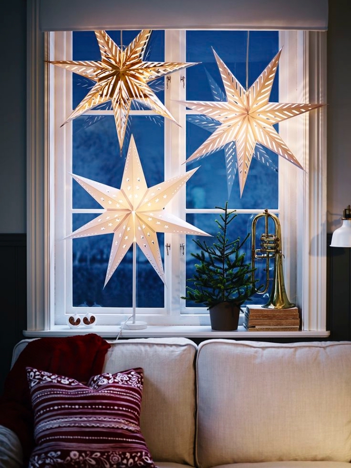 idee deco noel a faire soi meme, grandes étoiles lumineuses en papier suspendues à la fenêtre derrière le canapé
