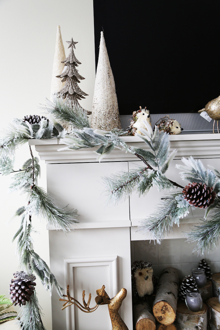 photo fausse cheminée décorative avec manteau blanc cassé avec décoration noel avec guirlande de sapin artificielle pommes de pins de buches de bois dans le foyer