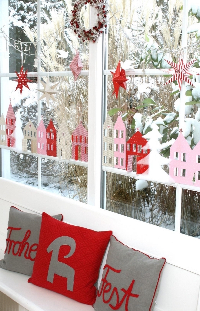 de petites silhouettes de maisons découpées en papier rose et rouge pour décorer la vitre à Noëln guirlande d'étoiles en papier suspendue à la fenêtre en dessus un banc blanc