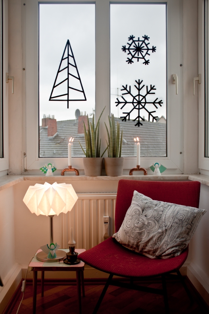 décorer les vitres avec un sapin de noël original et des flocons de neige en masking tape, coin de lecture décoré pour l'hiver avec un fauteuil rouge et une petite table d'appoint illuminée par une lampe à poser origami