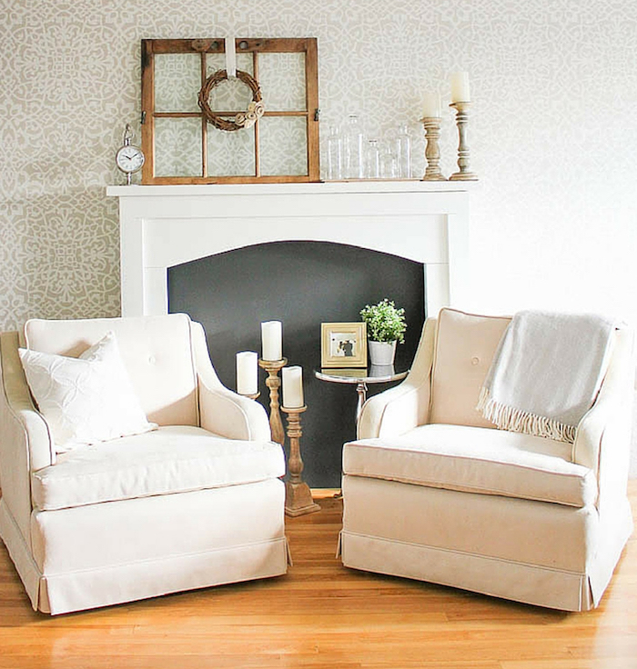 photo salon déco minimaliste avec cheminée décorative à fond noir et objets déco rétro, fauteuils en tissu clair, sol parquet et tapisserie gris blanc