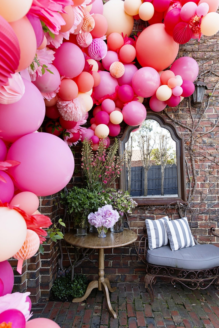 décoration d'extérieur pour fêtes et mariages, multitude de ballons roses liés ensemble en guirlande décorative, maison ancienne, petite table d'extérieur et canapé en fer forgé