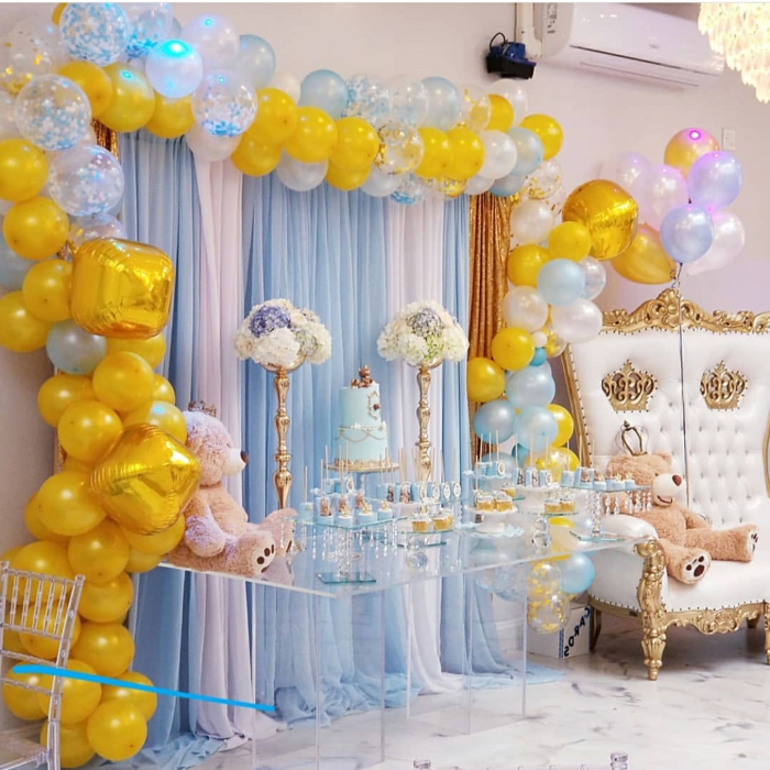 table acrylique, grand fauteuil baroque avec ours beige, arche ballons jaunes et bleus, gâteau bleu, plafonnier en cristal